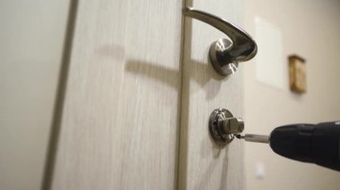 Yakın plan. Carpenter eve kablosuz tornavida kullanarak kapı kilidi kuruyor, son işlem. İnşaat endüstrisi. Anahtarlı yeni bir kapı kilidi takıyorum. Görüntü