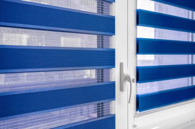 Dark blue fabric roller blinds on the plastic window in the living room. Duo system day and night, detail. Sunshine shutters mounted on window and balcony door. Modern jalousie clipart