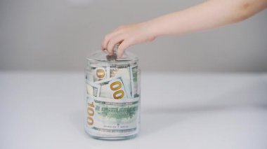 Yakın plan Childs 'ın eli 100 dolarlık banknotlarla dolu bir kavanoza bir dolar koyar. Finansal okur yazarlık kavramı, geleceğe yatırım