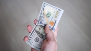 100 dolarlık banknotlarla yakın plan erkek eli. Adam banknotları ve kıskaçları para klipsiyle katlıyor. Para ellerinde.