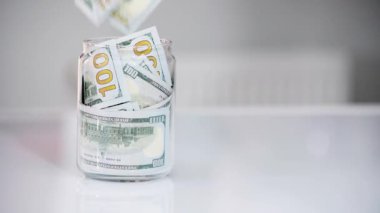 Cam kavanozdaki dolarlar. Erkeklerin kavanoza dolar koymalarını izlemek. Evde para biriktirme kavramı. Tasarruf kavramı finans ve yatırım. Yavaş çekim