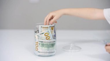 Yakın plan Childs 'ın eli 100 dolarlık banknotlarla dolu bir kavanozdan para çalar ya da çeker. Küçük zengin adam. Finans ve başarı iş konsepti