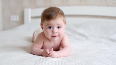 Sevimli küçük erkek bebek karın üstü yatıp kafasını tutmayı öğreniyor. Bebek bezli güzel bir bebeğin portresi. Ağzı açık kameraya bakıyor.