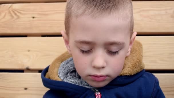 Allvarlig drömmande liten pojke med slutna ögon. Han öppnar ögonen. Ansikte utomhus porträtt närbild. Träbakgrund — Stockvideo