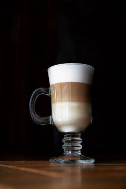 Siyah arkaplanlı cam bardakta kahve. Koyu arkaplanda üç katmanlı latte. Siyah arkaplanlı cam bardakta kahve. Sütlü kahve. Dikey çekim