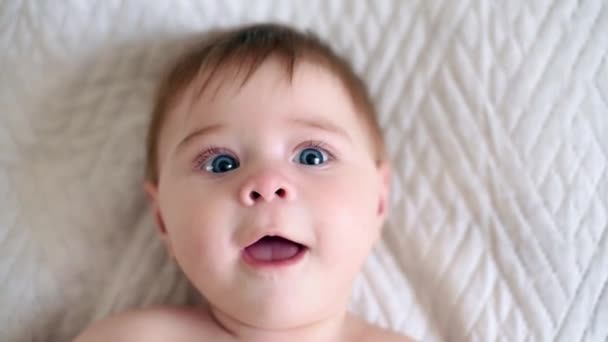 Funny infant baby boy looks at his hand with surprise. Close up portrait view — Stock Video