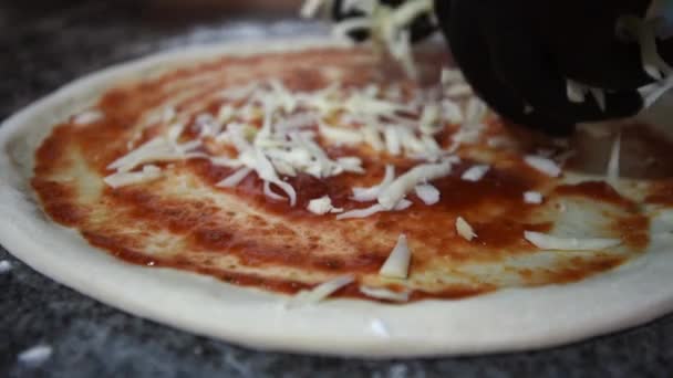 Bir şef ev yapımı, rendelenmiş peynirli pizza serper, yakın plan. Pizza hamurunun üzerine rendelenmiş parmesan peyniri ya da Maasdam peyniri koyan bir adamın eli. — Stok video