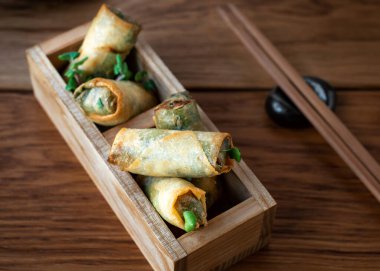 Asya mutfağı. Yumurta rulosunu yakın çekim dekoratif ahşap kutularda yemek çubuğuyla servis edilir. Kızarmış Çin böreği ve acı biber sosu. Asya aperatifleri veya atıştırmalıkları