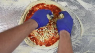 Lastik eldivenli üst manzara elleri pizza hamuruna taze rendelenmiş peynir serpiyor. Şef pizza pişiriyor.