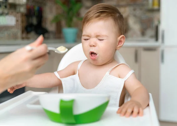 迷人的8 11个月大的小男孩不想和妈妈在家里用勺子吃粥 孩子不喜欢吃东西 没胃口不幸的孩子 — 图库照片