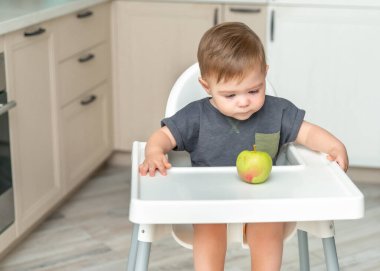Meraklı bir bebek faiziyle elmaya bakıyor. Çocukluk konsepti, ilk yem ve bebek maması. Bebeğin ilk yemi.