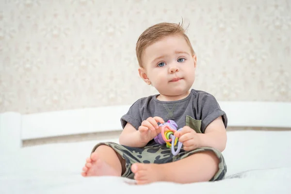 Sorrindo menino caucasiano em shorts e t-shirt brincando com brinquedo chocalho colorido. Atividades para bebês. Bebê segurando um brinquedo Fotografia De Stock