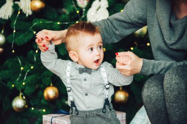 Anne ve oğlu Noel Ağacı 'nın yanında duruyor. Noel ağacına karşı papyon ve gömlek takan süpriz bir erkek bebek.