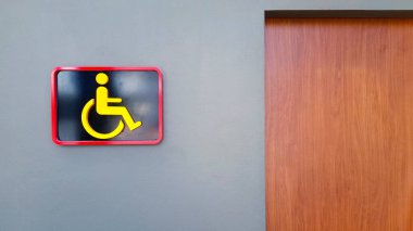 Gri ya da gri duvardaki tuvalet tabelasında sakat insanlar için bu tuvaleti sadece fotokopi alanı olan bir yer olarak kullanırlar. Umumi tuvalet mi yoksa tekerlekli sandalyedeki sakat mı? Nesnenin tasarımı ve şekli.