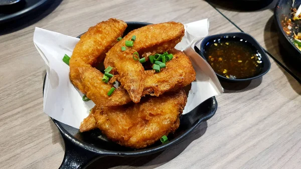 Salted deep fried wing chicken in black hot pan, dish or plate on with sweet or spicy sauce on wooden table at Thai restaurant. Asian food and Delicious crispy meal.