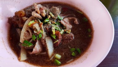 Tayland pirinçli erişteyi sığır eti, bayat et, ciğer, inek bezi, sakatat ve kahverengi ahşap arka planda veya masada kapayın ve yerel sokak yemeklerinin olduğu yere kopyalayın. Pembe kase üzerinde düz bir Asya yemeği yatağı.