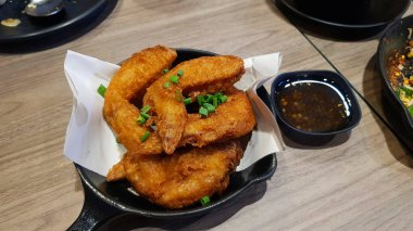 Tuzlanmış kızarmış tavuk ve siyah sıcak tava. Tayland restoranındaki ahşap masada tatlı ya da baharatlı sos. Asya yemekleri ve lezzetli çıtır yemekler..
