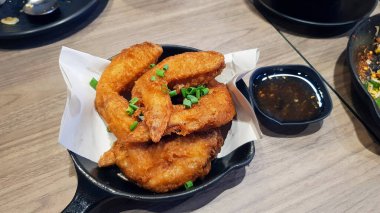 Tuzlanmış kızarmış tavuk ve siyah sıcak tava. Tayland restoranındaki ahşap masada tatlı ya da baharatlı sos. Asya yemekleri ve lezzetli çıtır yemekler..