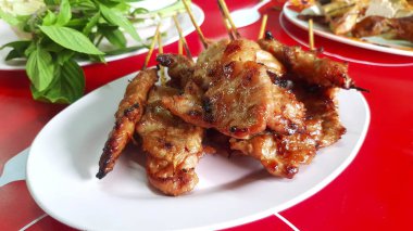 Tayland usulü ızgara domuz eti şişleri ya da kırmızı masa üzerinde bulanık fesleğen, kekik yaprağı, sebze ve yerel sokak yemeklerinde diğer yemek çeşitleri. Asya yemekleri ve lezzetli yemekler..