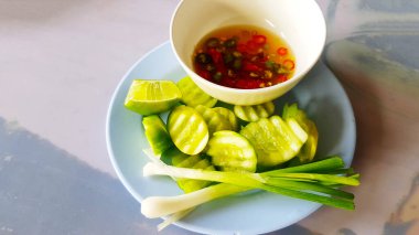 Taze salatalık, limon, taze soğan ve kırmızı ve yeşil biberli balık sosunu beyaz kaseye koy. Kızarmış pilav ve taze sebzeler..
