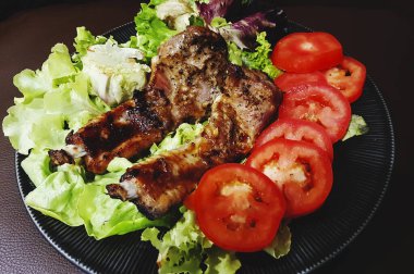 Izgara pirzola bifteği, taze domates, yeşil lahana ve siyah tabakta ıspanak. Sebzeli domuz barbeküsü..