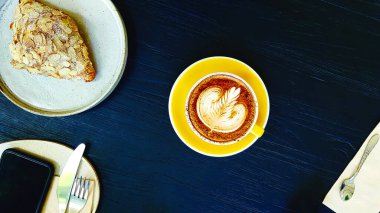 Kremalı badem kruvasan, bıçak, çatal ve telefonlu latte kahvenin mavi ahşap arka planda ve kafede fotokopi alanı var. Sıcak kapuçino içiyorduk. Sabahları dinlenme zamanı.