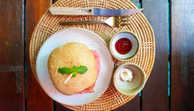 Domates soslu beyaz tabak üzerine jambon ve çizburger, mayonez sosu, çatal ve bıçak kahverengi ahşap arka planda dokuma tepsisinde. Amerikan ya da abur cubur manzarası. Sabah yemeği