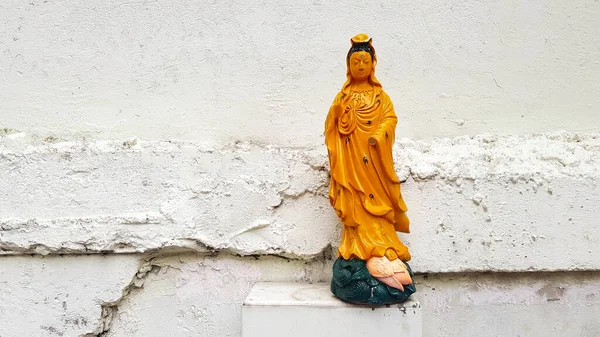 Yellow Goddess of Guanyin or Mercy statue putting stainless steel box with white rough or grunge concrete wall background and copy space. Asia Religion, Faith, Belief and Damaged of art object