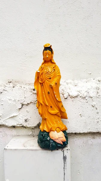 Yellow Goddess of Guan Yin or Mercy statue putting stainless steel box and hand broken on white rough or grunge concrete wall background. Asia Religion, Faith, Belief and Damaged of art object.