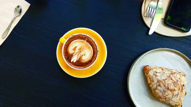 Kremalı badem kruvasan, bıçak, çatal ve telefonlu latte kahvenin mavi ahşap arka planda ve kafede fotokopi alanı var. Sıcak kapuçino içiyorduk. Sabahları dinlenme zamanı.