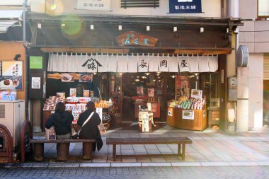 Japonya - 22 Şubat 2019: Japonya 'da Takayama, Japonya' da sokak yemeklerinden alışveriş yaptıktan sonra iki kadın ya da arkadaş vestiyer önünde oturuyorlar ve konuşuyorlar. Ziyaret veya seyahat için simge