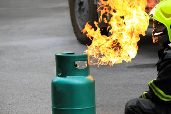 Fire burning on green gas container. and Firefighter or fireman in black uniform and wearing safety helmet try to extinguish the fire on street with car wheel background and copy space. Conflagration