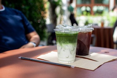 Yeşil Matcha Latte ve kafe bahçesindeki masada plastik bardakta kahve..