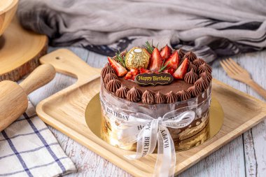 Chocolate cake decorated with strawberry and white ribbon for birthday cake on wooden board.