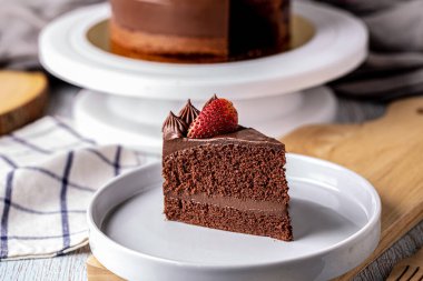 Slice of delicious homemade chocolate cake soft fudge topping with strawberry on white plate.