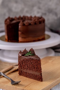 Slice of delicious homemade chocolate cake soft fudge paste on wooden board with fork for serve.