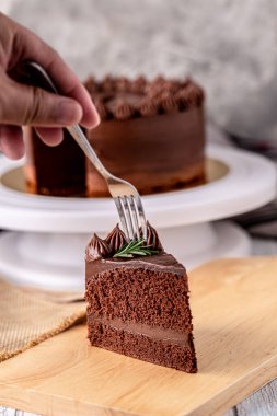A young man holding a fork for eat a delicious chocolate cake on wooden board on table.