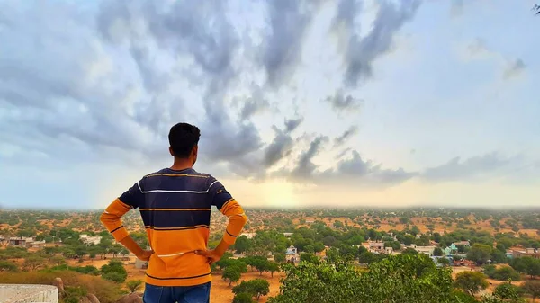 Genç Hintli adam ayakta ve elleri belinde dağda yere bakıyor.