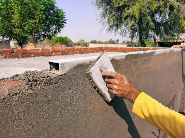 Mason duvardaki beton alçıyı bitiriyor ve elle düzleştiriyor.