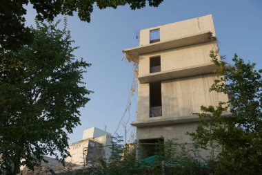 Çelik kablolar ve kablolar kısmen parçalanmış beton bina kabuğundan çıkar. Yumuşak sabah güneşi ve mavi gökyüzü arkaplanı. Yapraklı bitki sınırı.