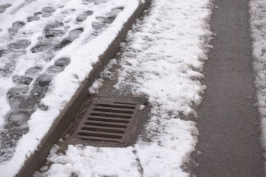 3 - Winter road scene with surface storm drain receiving the heavy water run off. Part of the december season weather in britain, bringing flood risk clipart