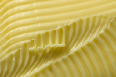 Sarı tereyağını kapat. Süper makro perspektifli, dokulu arka plan. Soyut desenleri oluşturmak için kullanılan tırtıklı tereyağı bıçağı.