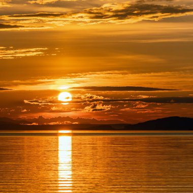 Umea Nehri Dağları üzerinde Sunset 'in kare fotoğrafı, turuncu kırmızı güneş tarafından aydınlatılmış bulutlarla dolu yaz gökyüzü. Su üzerindeki güneş ışığı yolu Storuman, Laponya, İsveç