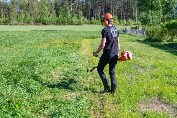 Teenage Boy going to cut grass with handheld gasoline lawn mower. He wears eye and ear protection headphones. Health and safety concept, worker job protection.Safe work conditions