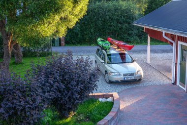 UMEA, SVEDEN - 1 Haziran 2021: Umea şehrinin ağaçlarının altındaki garaja yakın özel otoparkta iki atlı kanosu olan bir yönetici arabası. Güneşli sıcak bir gün. Yeşil ve kırmızı kanolar. Kuzey İsveç