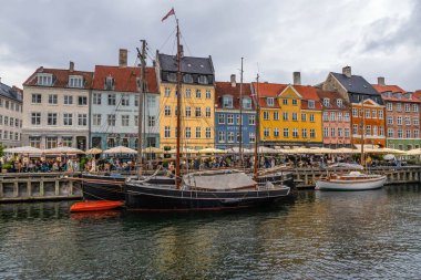 Nyhavn kanalı canlı bir manzara oluşturuyordu. Rıhtım boyunca çok sayıda tarihi tekne yanaştı ve 17. yüzyılın renkli konak evleri kalabalık restoran ve kafelere ev sahipliği yapıyordu. Kopenhag, Danimarka 12 Temmuz 2025