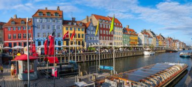 Kanal kenarında dinlenen turistler, canlı Kopenhag şehrinde tarihi evler ve tekneler yakınında açık havada yemeğin tadını çıkarıyorlar. Kopenhag, Danimarka 13 Temmuz 2025