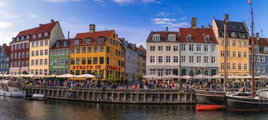 Nyhavn limanını çevreleyen renkli cephelerde açık hava restoranlarında dinlenen insanlar ve kanala yanaşmış tarihi tekneler. Kopenhag, Danimarka 13 Temmuz 2025