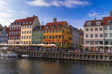 Kopenhag 'daki Nyhavn rıhtımında uzanan renkli tarihi binalar. İnsanlar açık hava yemeklerini ve tekne aktivitelerini seviyor. Kopenhag, Danimarka 13 Temmuz 2025