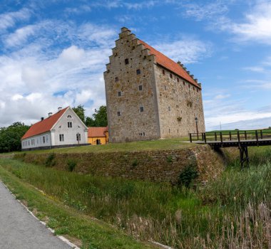 Glimmingehus kalesi. Skane 'de iyi korunmuş bir ortaçağ kalesi. Hendeği olan bir yaz gökyüzünün altında duruyor. Tahta köprü. Ve yakınlardaki geleneksel beyaz ek bina. Zamansız Avrupa mirasını yansıtmak